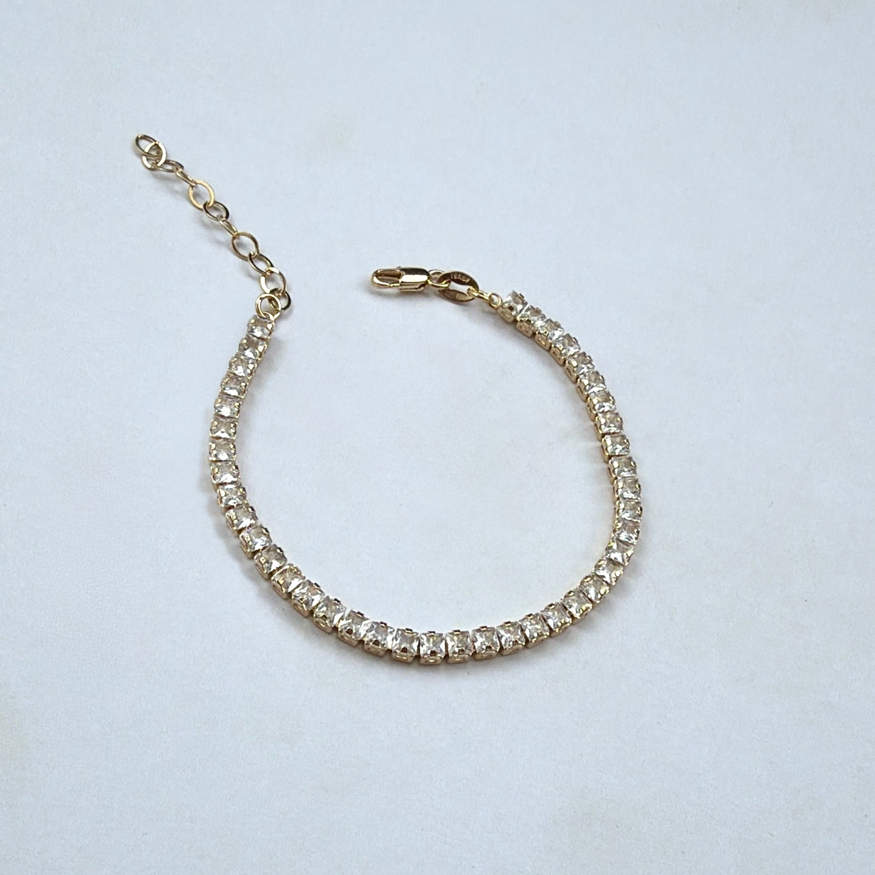 A delicate gold tennis bracelet adorned with clear round-cut stones, displayed on a light gray background.